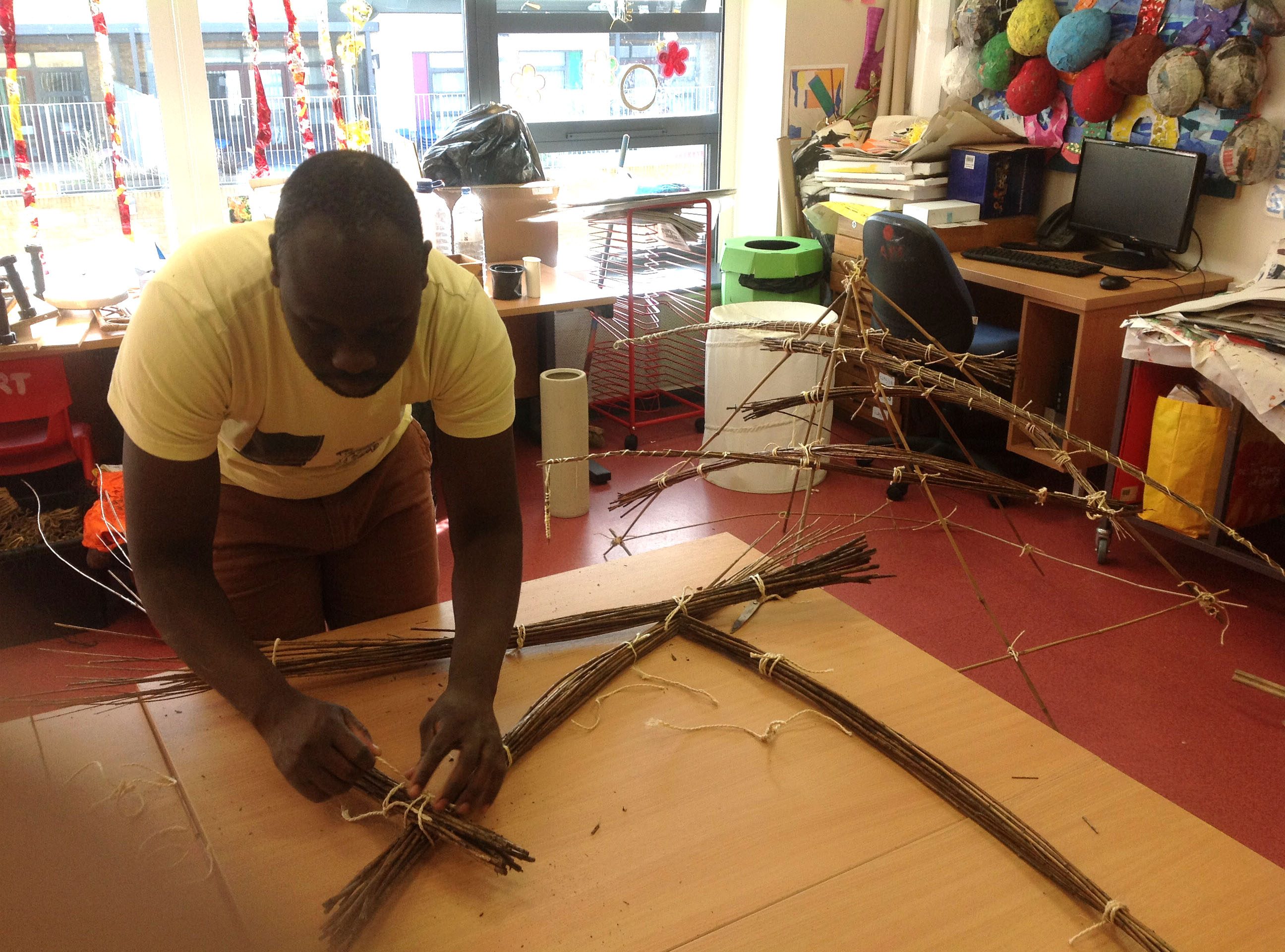 Artist Andrew Omoding tying bundles of willow sticks into a sculpture during a workshop at The Village School.