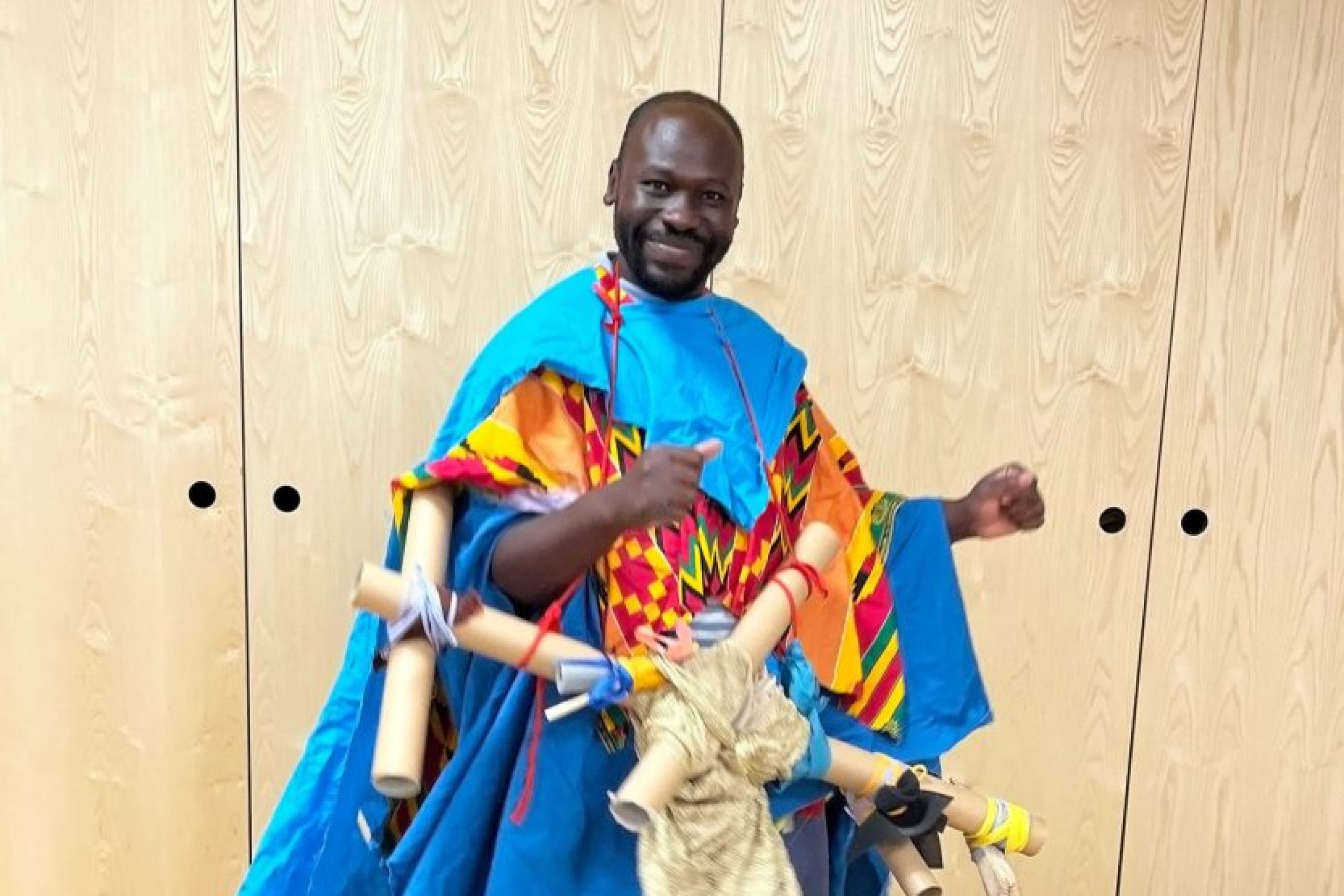 Andrew Omoding stands in a colourful blue outfit.