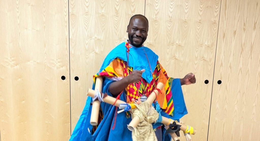Andrew Omoding stands in a colourful blue outfit.