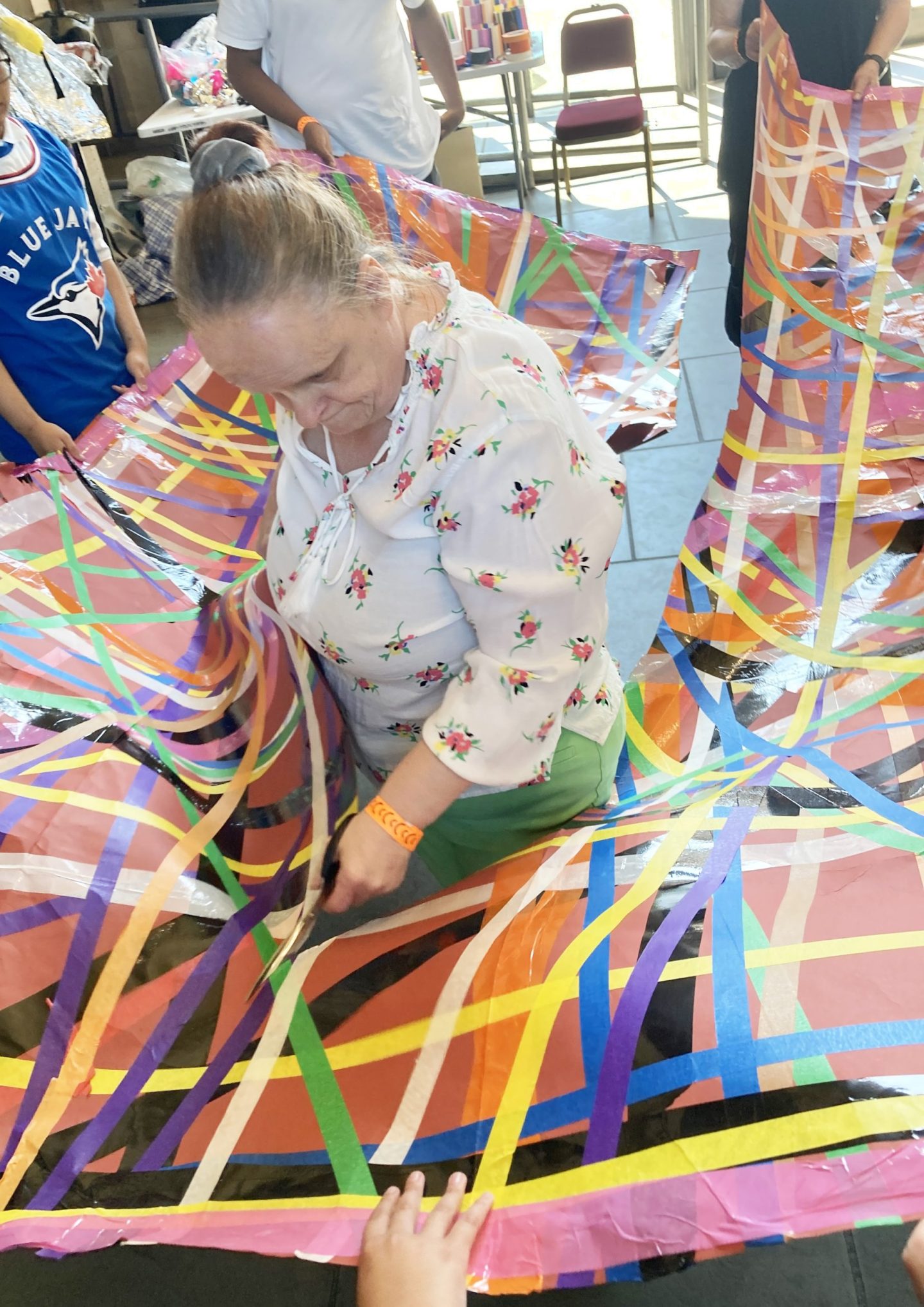 Linda Bell stands inside a large colourful sheet, with colourful tape all over it. Participants stand outside of the sheet, holding it at waist level.