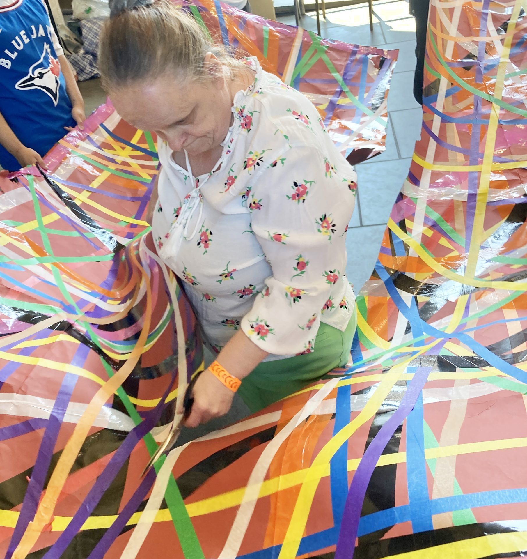 Linda Bell stands inside a large colourful sheet, with colourful tape all over it. Participants stand outside of the sheet, holding it at waist level.