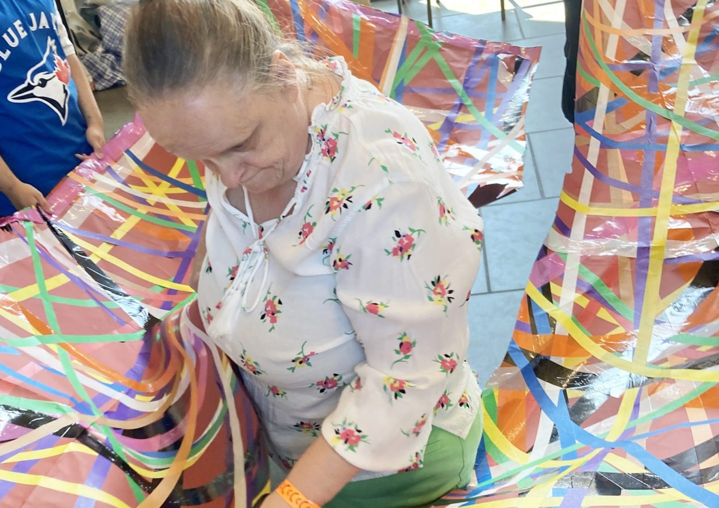 Linda Bell stands inside a large colourful sheet, with colourful tape all over it. Participants stand outside of the sheet, holding it at waist level.