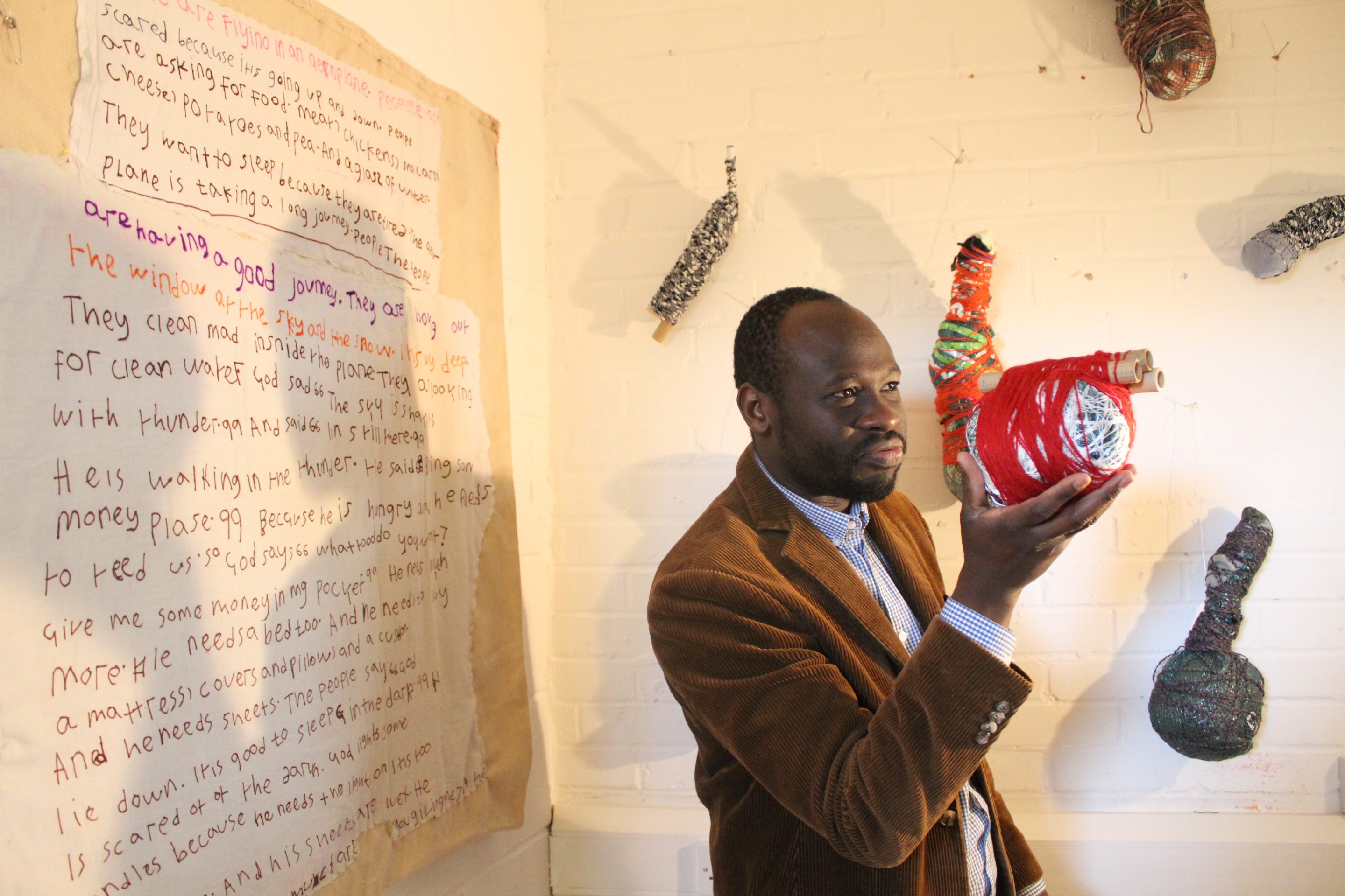 Andrew Omoding at Cockpit Arts Open Studios 2016, stood by his work and holding one of his sculptures in his right hand.