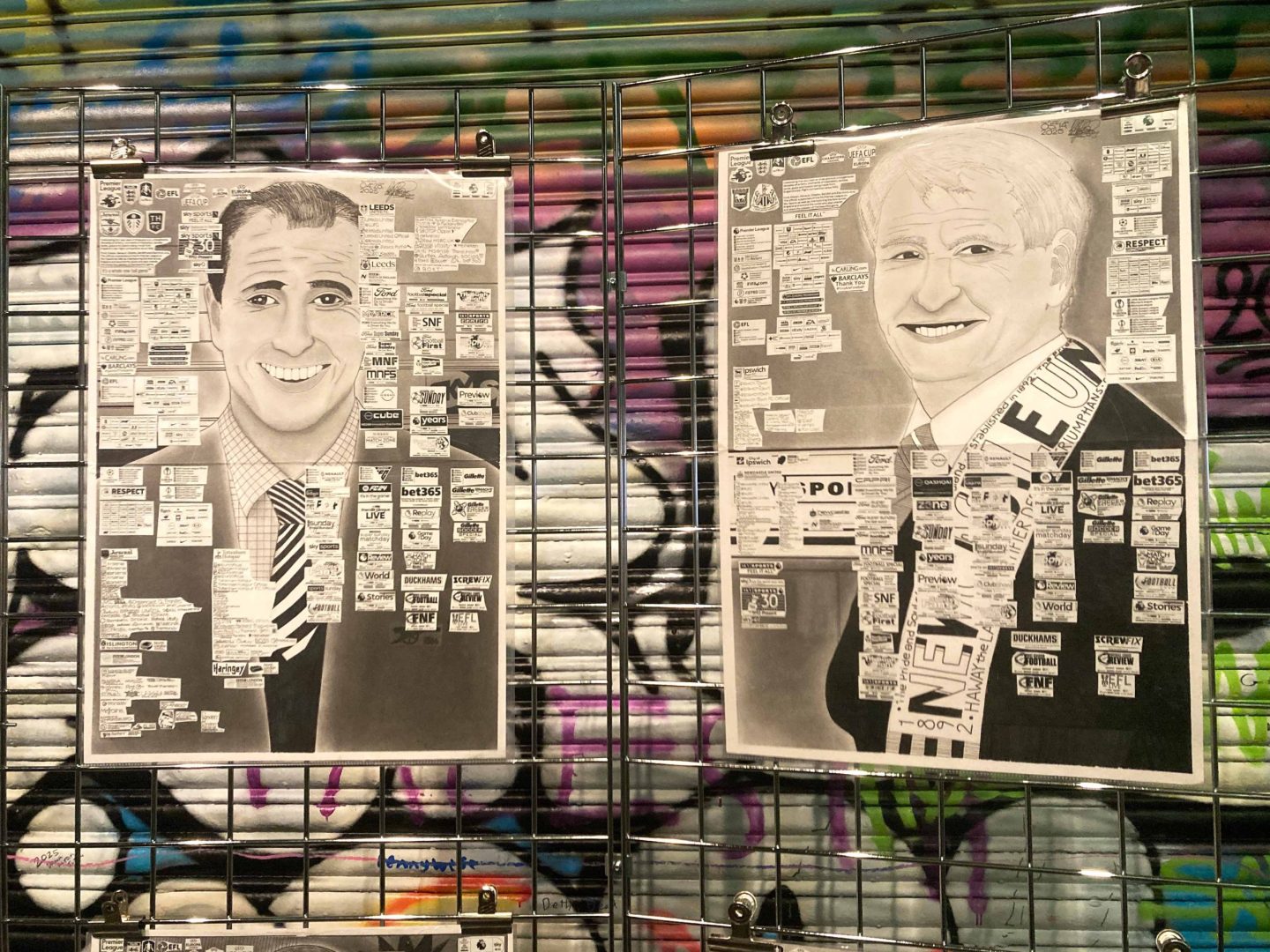 2 of Babajide's artworks hang from a metal grid, with a grafiti'd roller shutter behind.