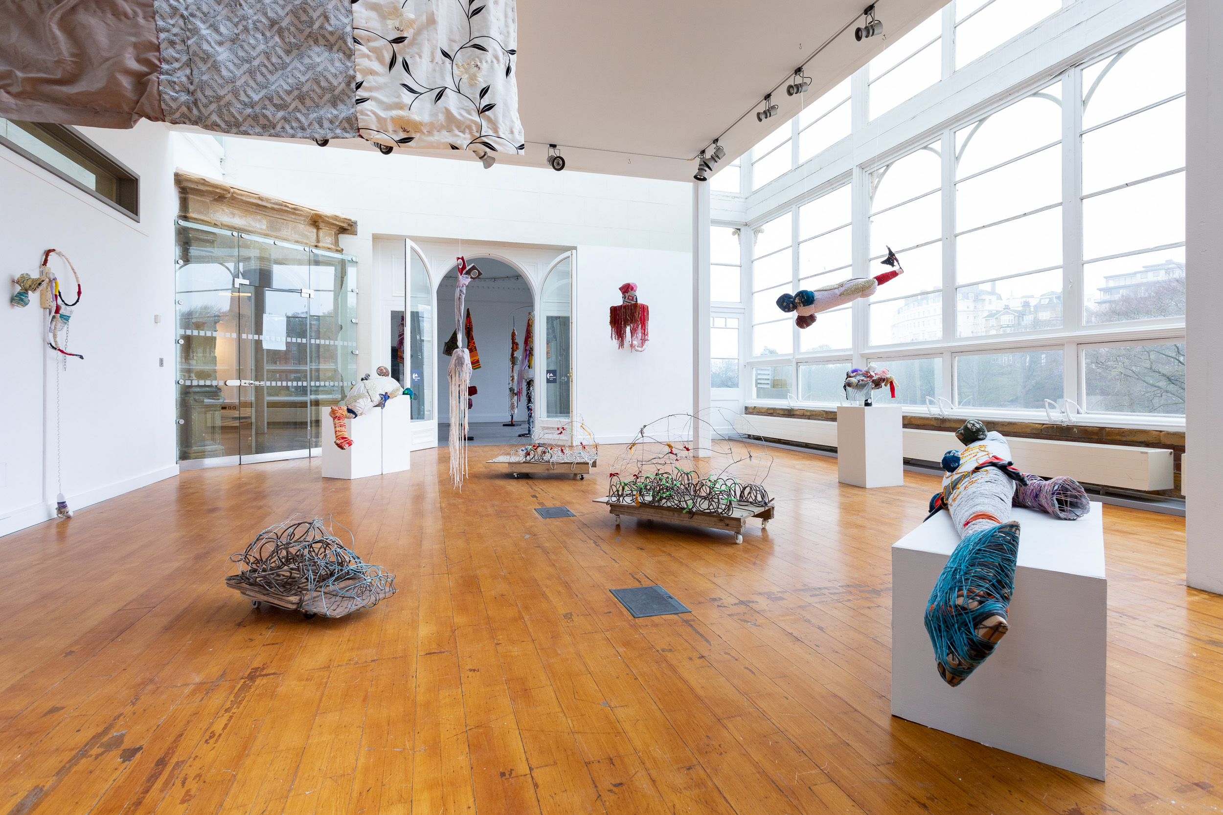 An exhibition space with multiple sculptures, some suspended from the ceiling, on plinths and the floor.