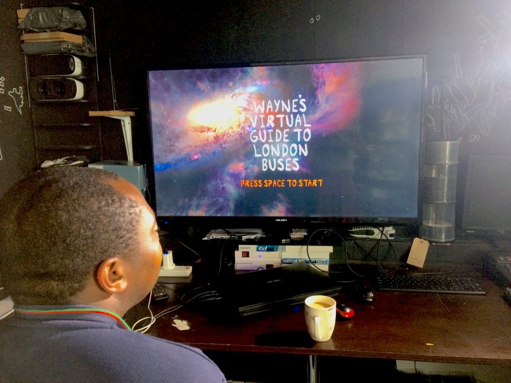 Wayne McGregor looks at a computer screen. The screen shows the cosmos, and in front white text saying 'Wayne's virtual guide to London buses'.