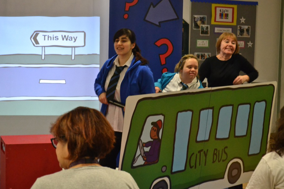 School children perform in a play, using a large cut out of a green city bus in their performance. The bus was illustrated by Declan Leslie.