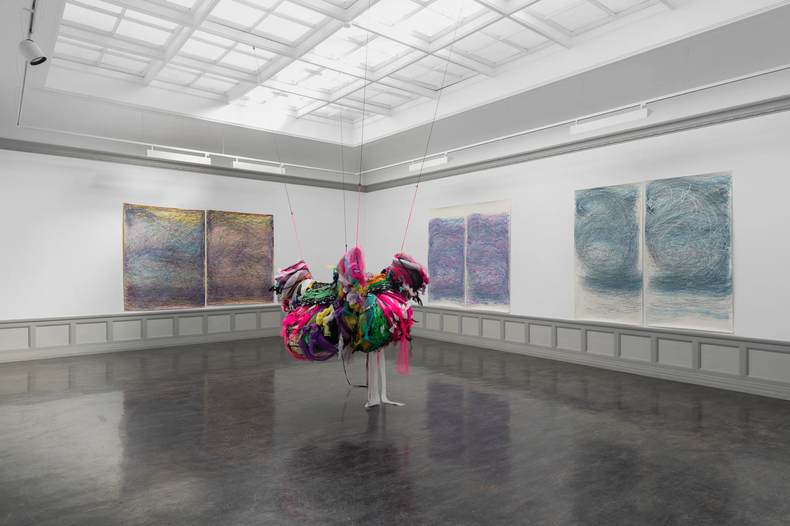A colourful mixed media sculpture hangs from the ceiling, 3 pairs of abstract drawings on the walls behind.
