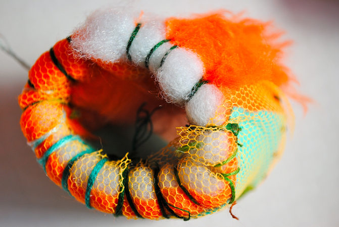 A detail of Lasmin's work. White and Orange stuffing is sewn together in a oval shape, with orange netting layered over.
