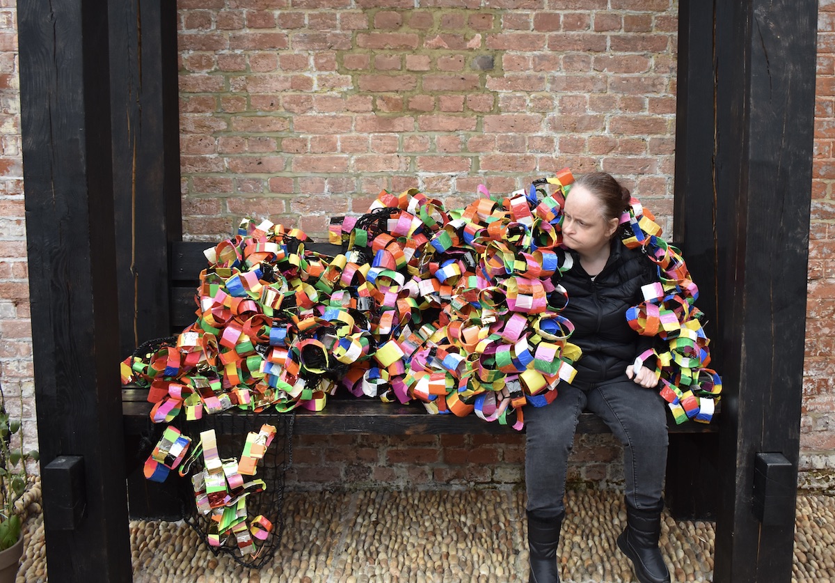 Linda Bell sits on a bench, her artwork of hundreds of colourful hoops attached together resting on her shoulders.