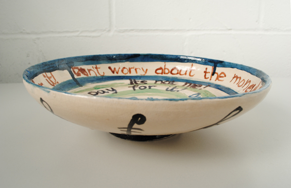 A ceramic bowl, with the inside and out painted by Matthew Berry. We can see the words 'dont worry about the money' on the inside.