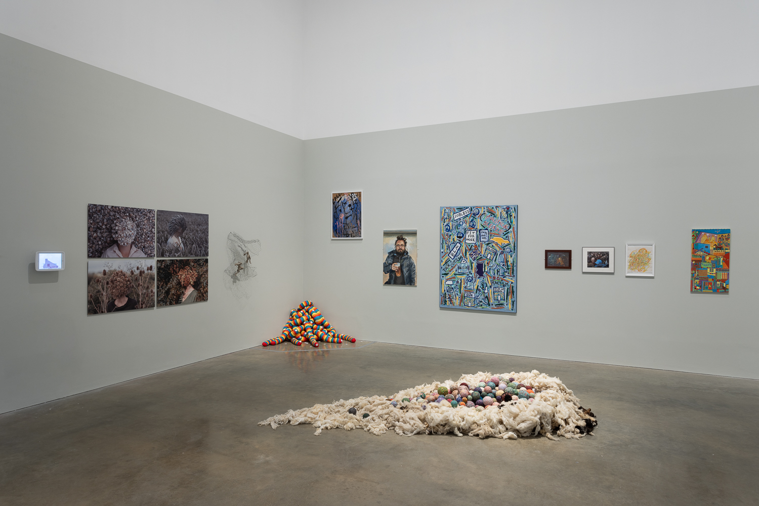 An exhibition with a fabric nest-like sculpture in the middle and rainbow fabric tentacles in the corner. On the walls, different artworks hang around a shared theme of identity.