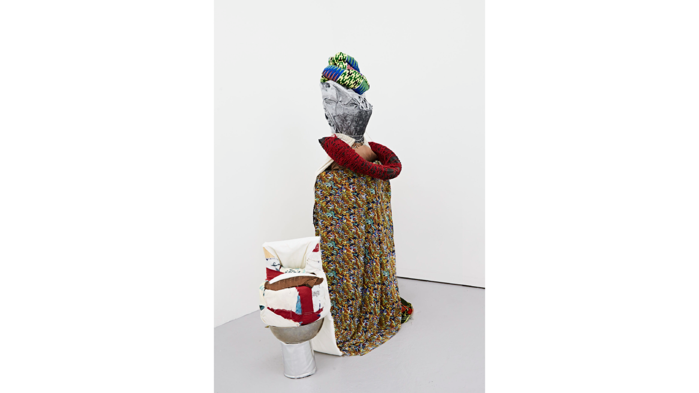 A multimedia textile soft sculpture in the form of a person draped in a cloak.