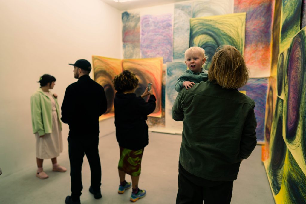 Visitors stand in a gallery space, with Nnena's work on the walls. A woman holds her baby.