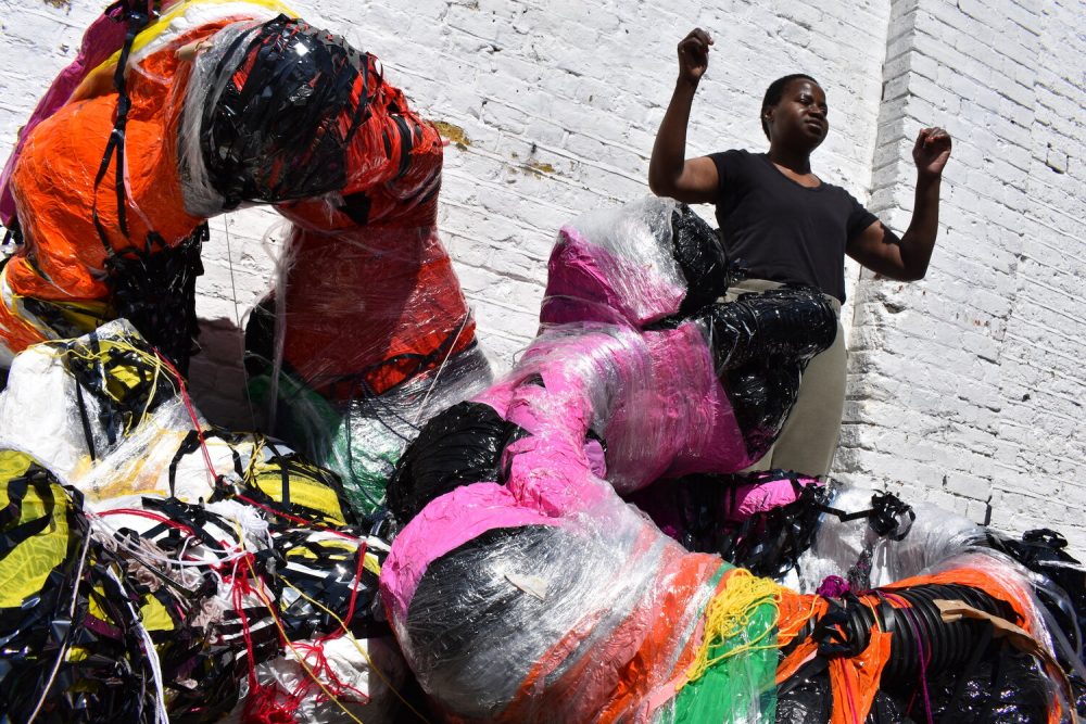 Nnena with one of her large sculptural works. The work is a large, tube like shape with colourful tape wrapped around it.