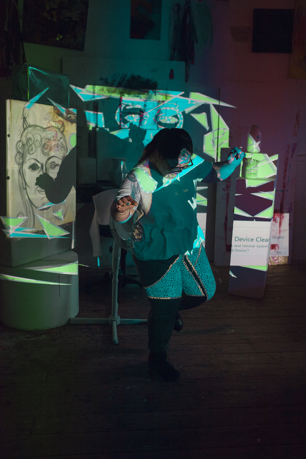 Ophir Yaron dances in front of a projector. The light is blue and behind her are different artworks.