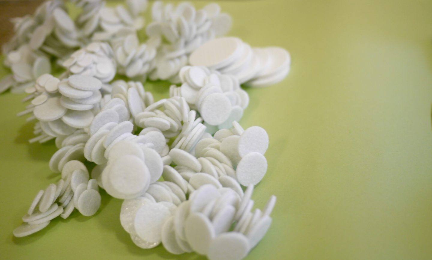 Close up of an artwork made of heaps of white circles of felt, on a green background.