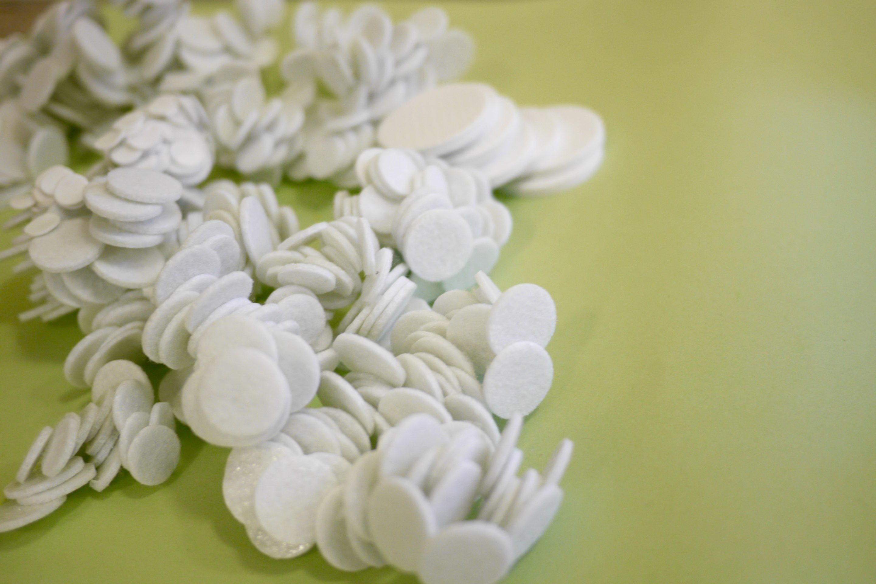 Close up of an artwork made of heaps of white circles of felt, on a green background.