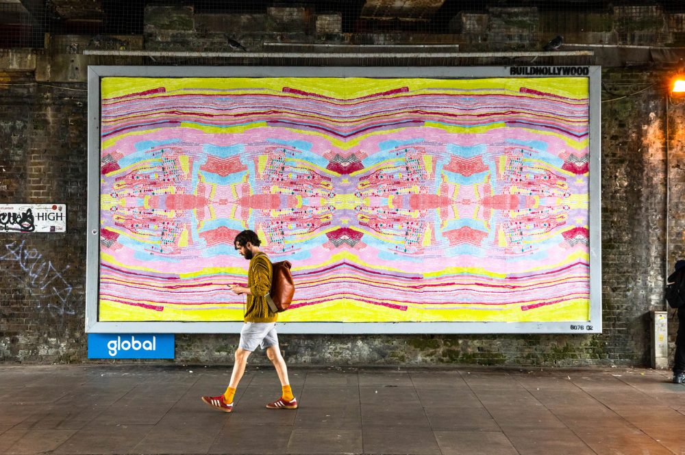 Jorell's artwork is on a billboard, and a man walks past it. The work is a colourful abstract piece of yellow and pink dots.