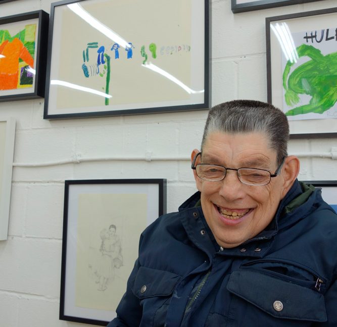 Artist Roland Young stood in front of a wall of framed artworks.