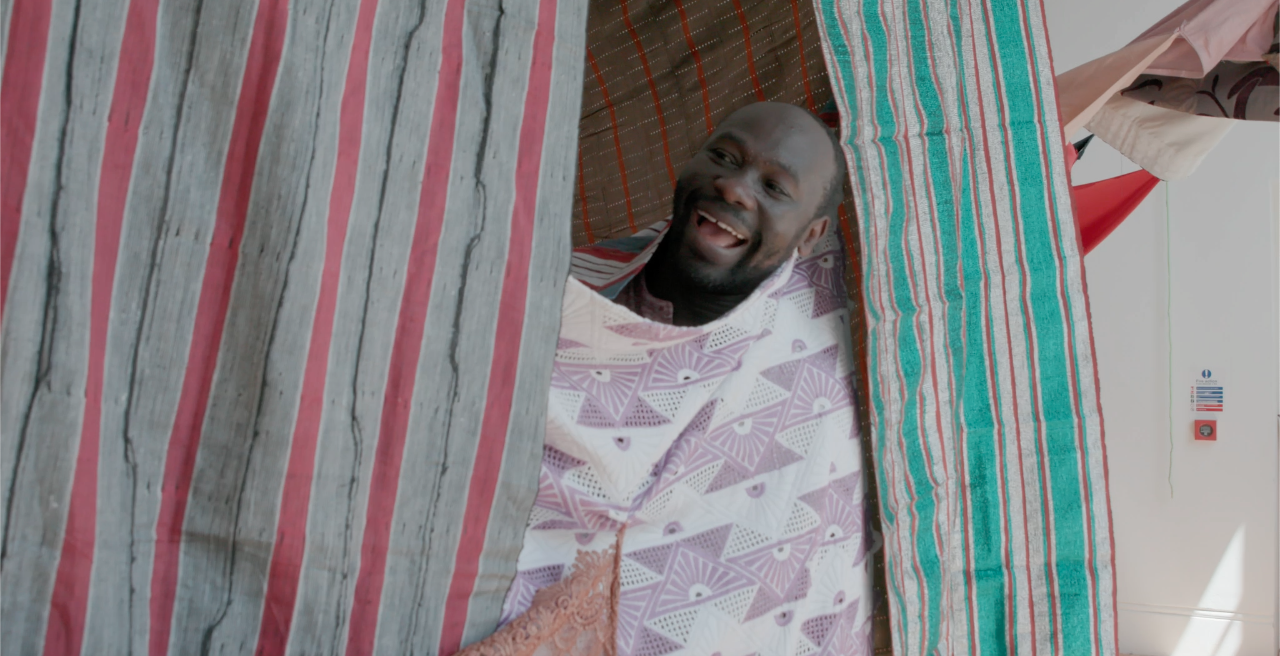 Artist Andrew Omoding inside a tent made of draped fabric.