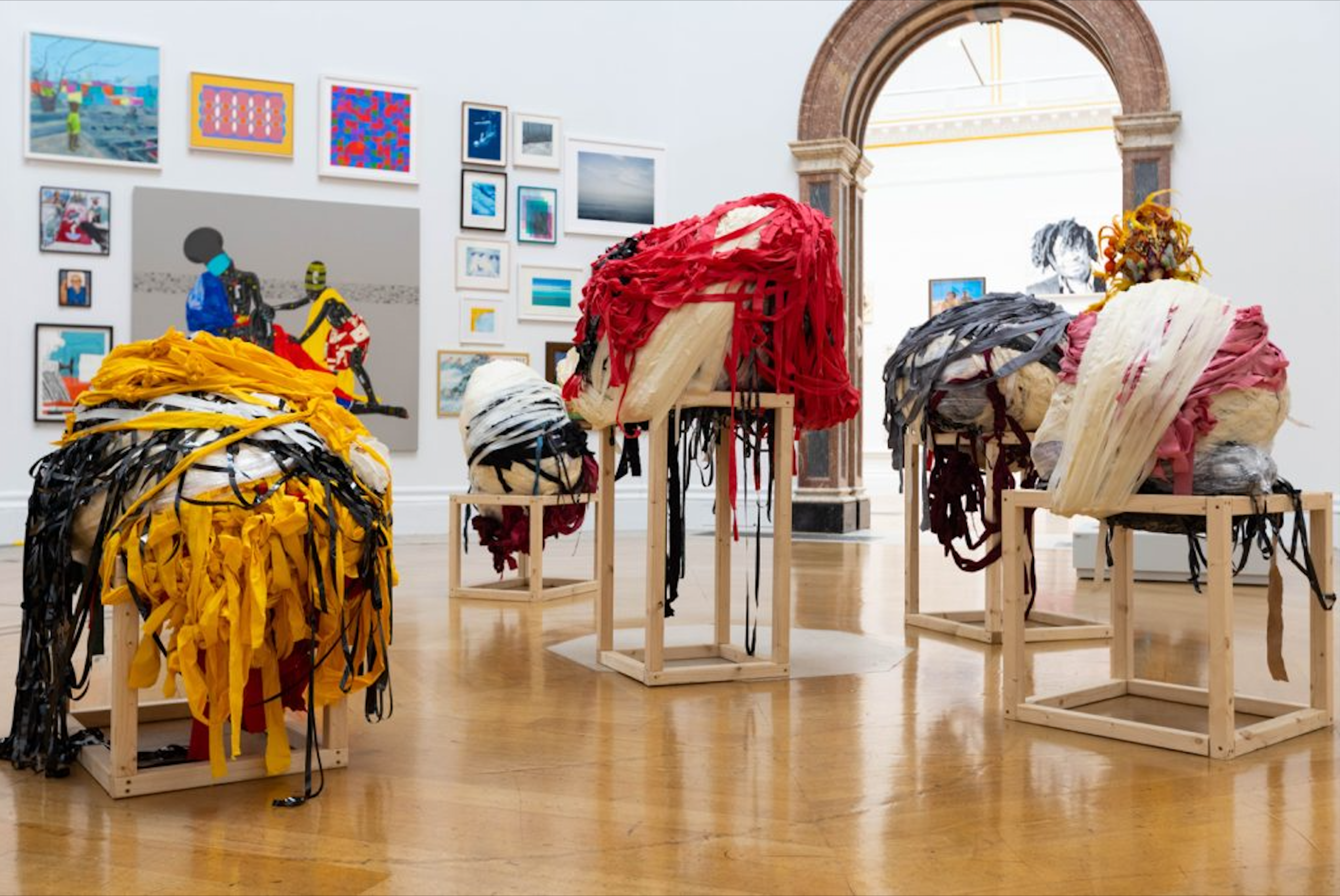 Nnena's work, in a gallery. There are 4 of her sculptural pieces on plinths, with artworks from other artists framed in the background.