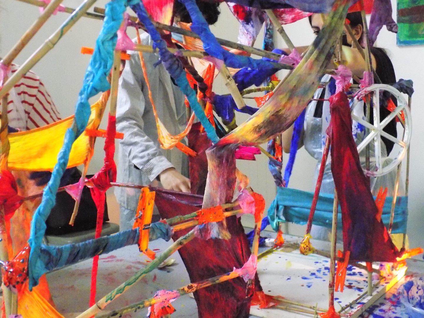 Close up of two people working on a sculpture made of bamboo sticks and dyed fabric.
