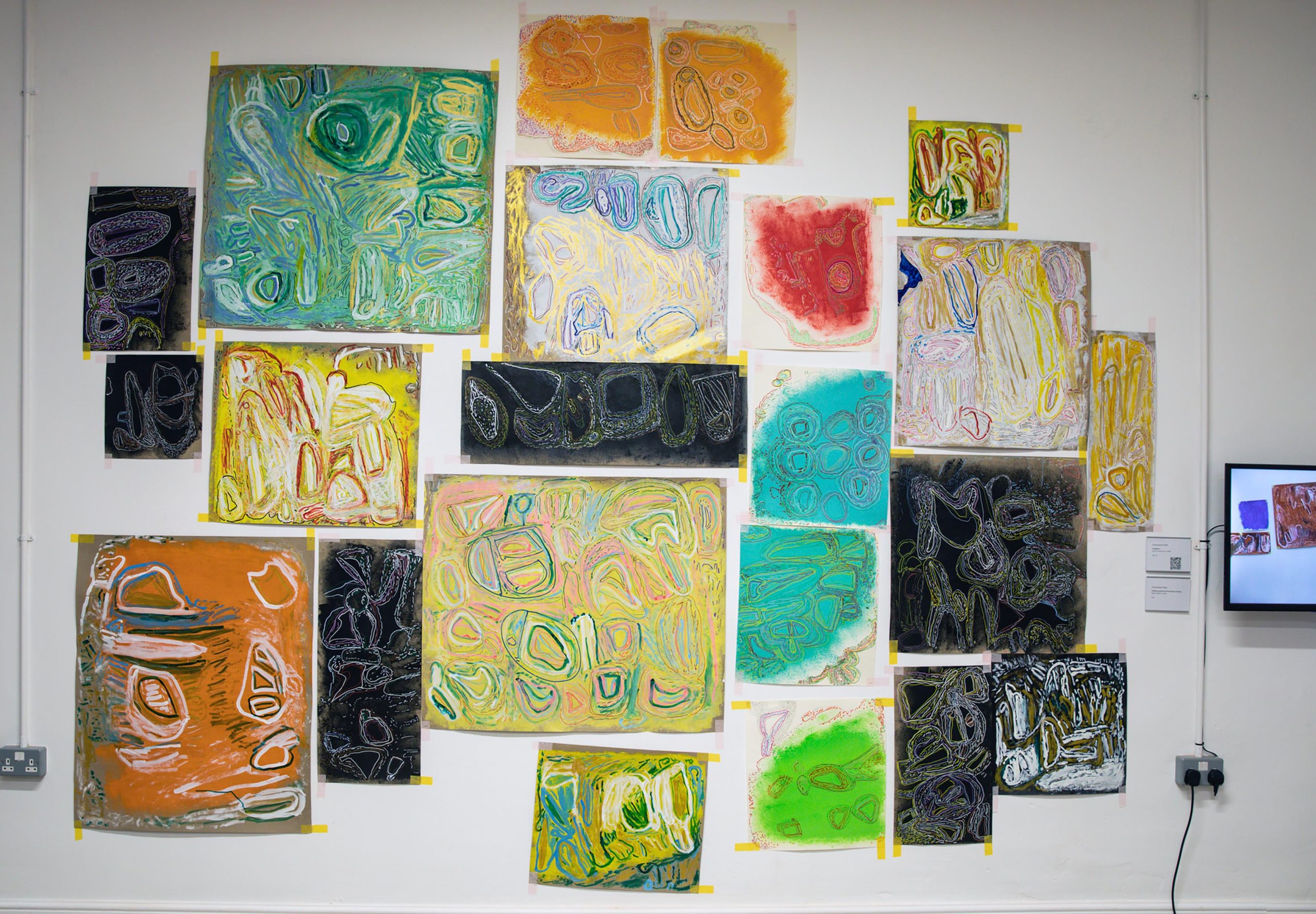 A wall of abstract pastel artworks stuck up with yellow tape.