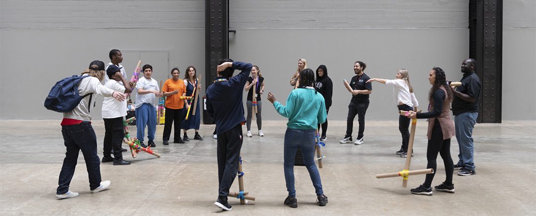 Andrew Omoding workshop with the public at the Tate. People are standing in a circle holding some of Andrew's artworks.