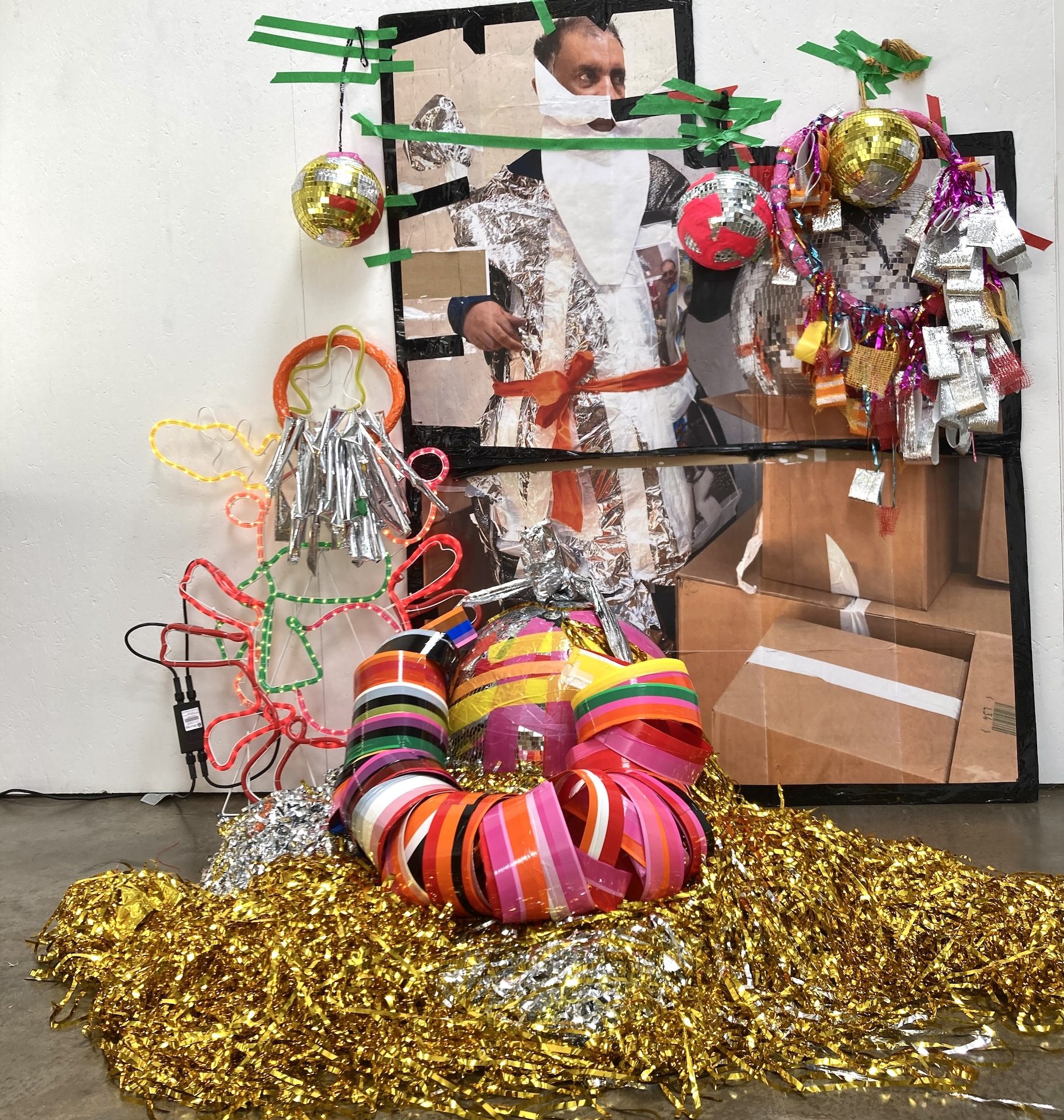 Pardip Kapil surrounded by one of his inhalations featuring tinsel, tape, a paper sant beard, disco balls and Christmas lights.