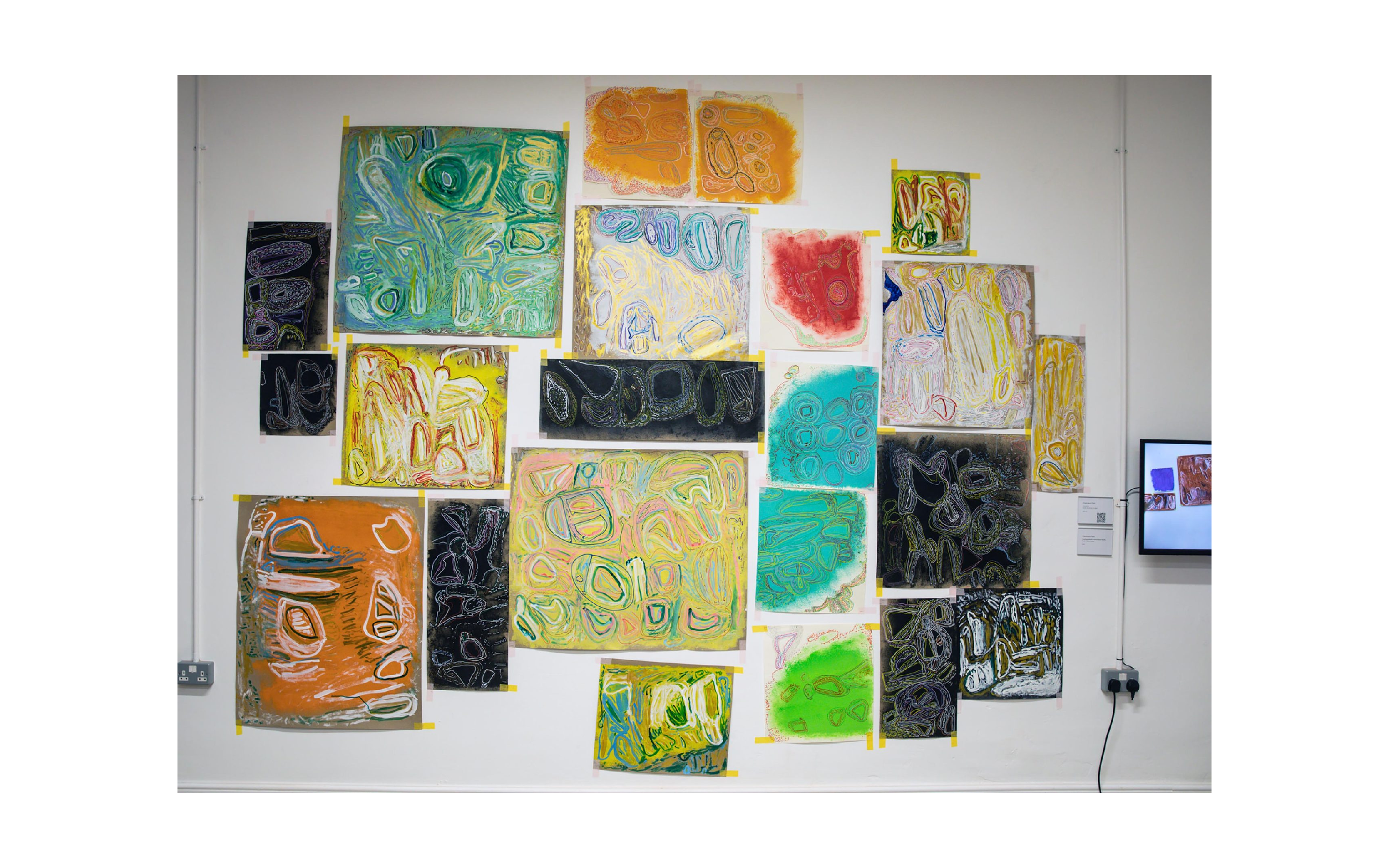 A wall of abstract pastel artworks stuck up with yellow tape.