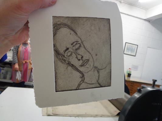 Jackie Murin holding up an etch print of a face in a printmaking studio.