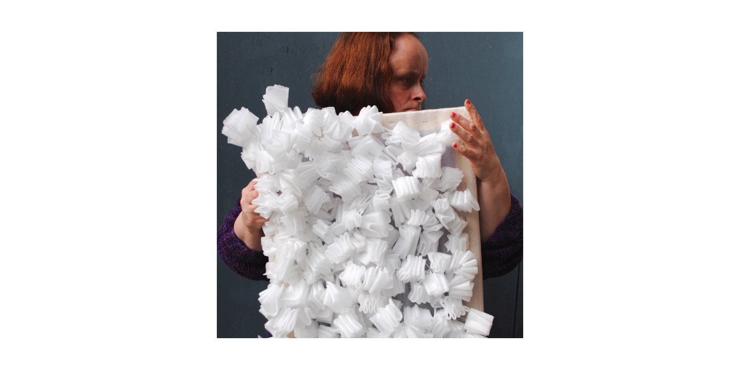 Artist Linda Bell holding up an artwork made of folds of polystyrene attached to a wooden frame.