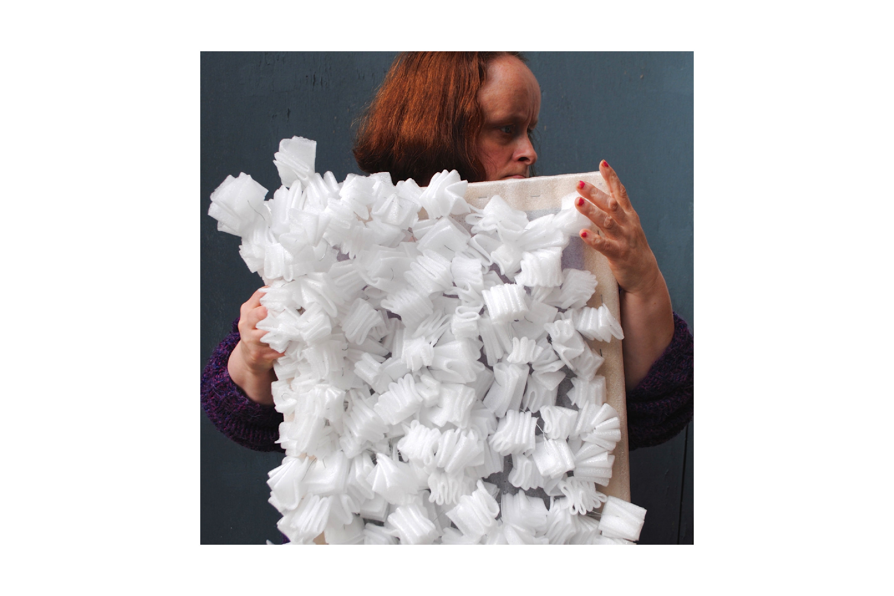 Artist Linda Bell holding up an artwork made of folds of polystyrene attached to a wooden frame.
