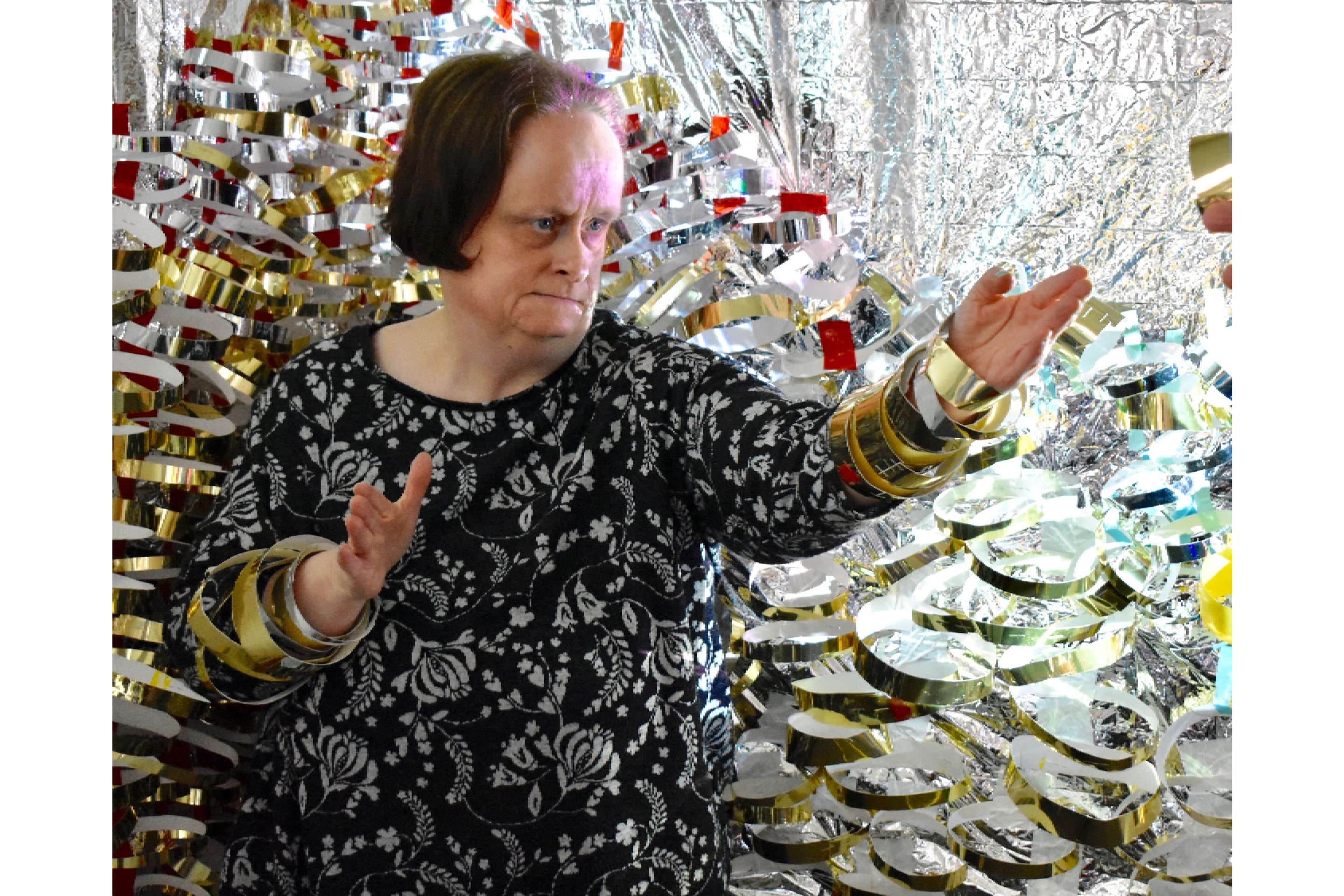 Linda Bell striking a karate pose next to her artwork wearing gold card loops around her wrists.