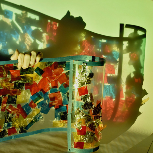 A sheet of transparent acetate covered in coloured paper with a light projecting through the work.