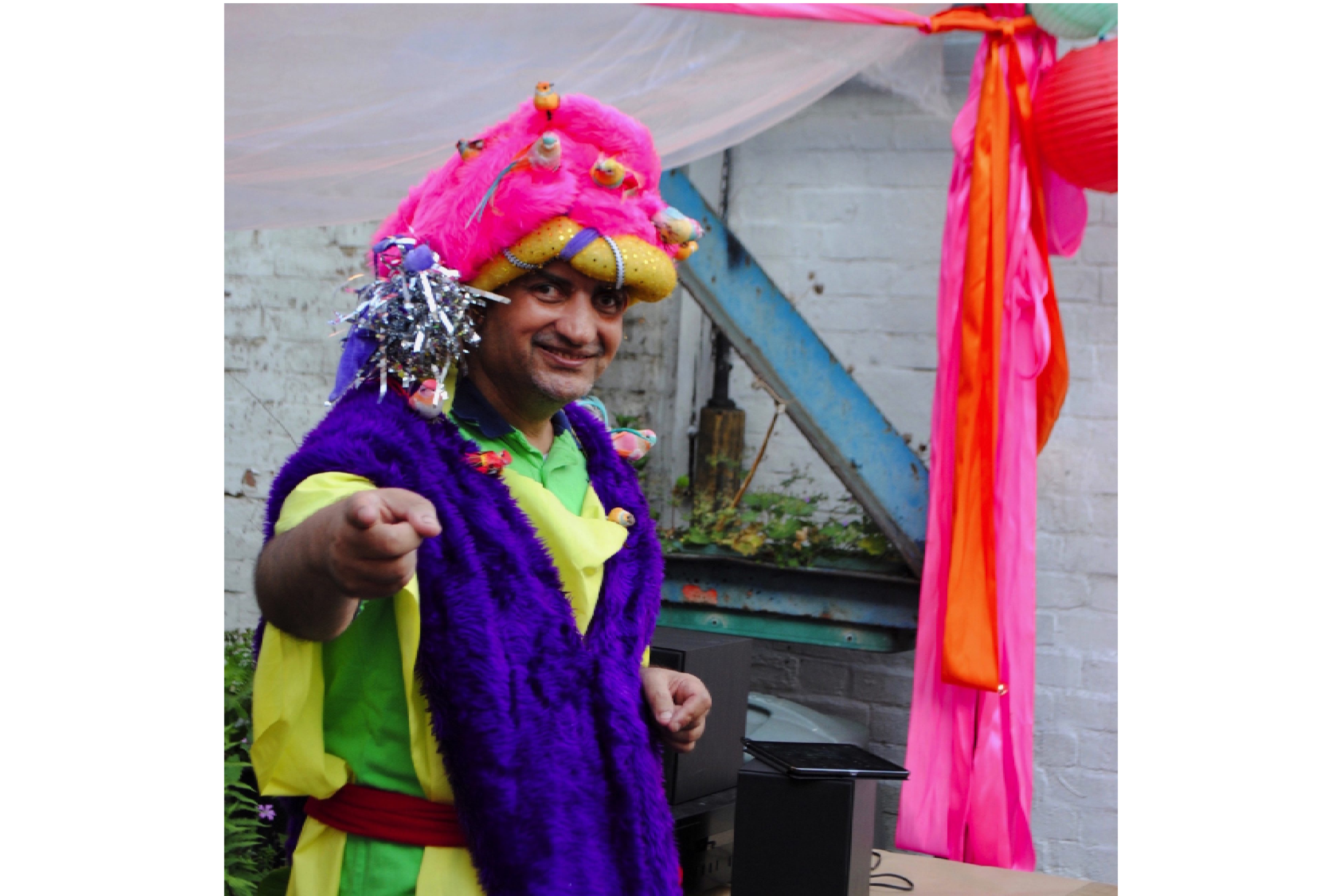 Artist Pardip Kapil wearing a DIY costume with a pink fluffy hat pointing towards the camera.