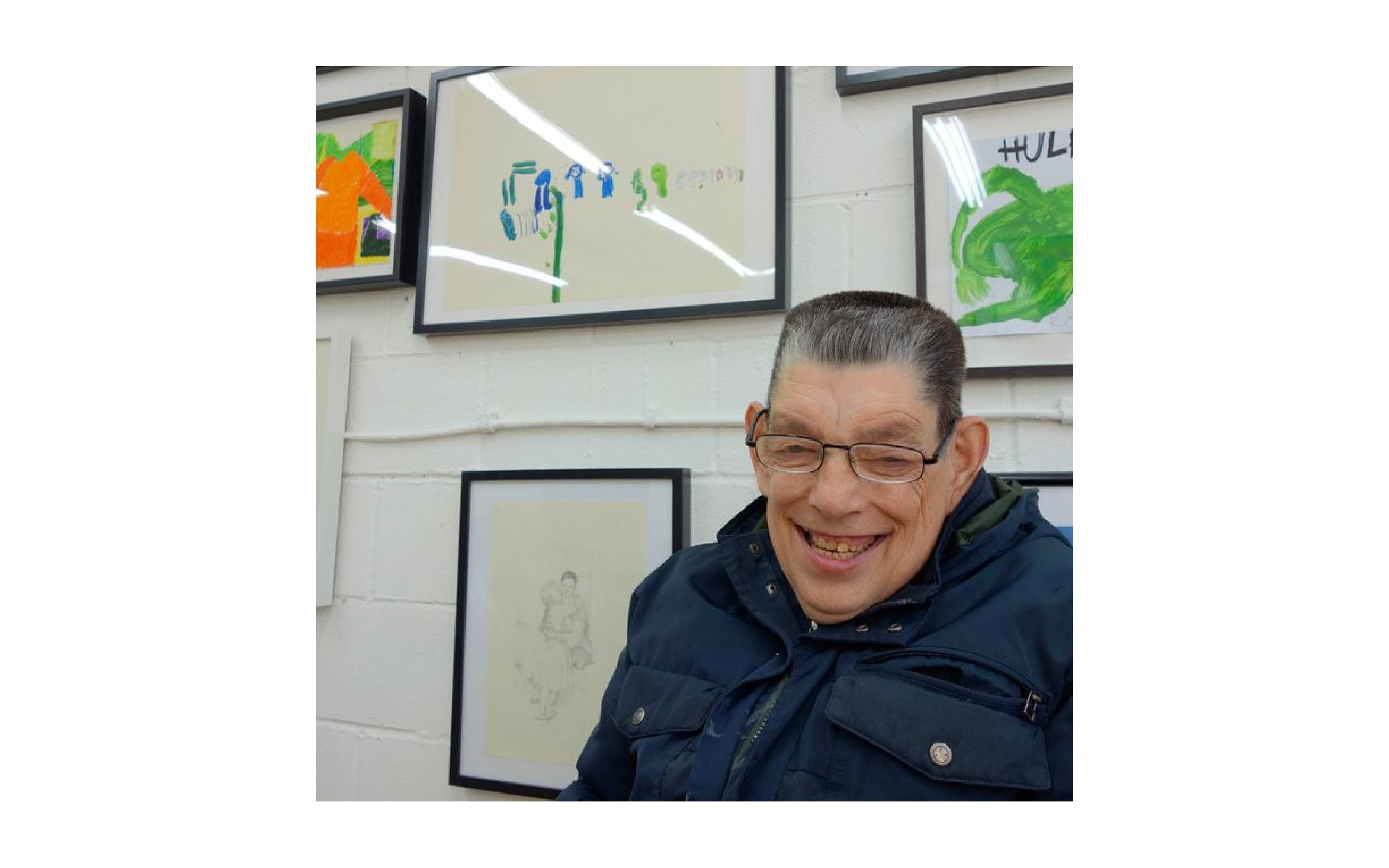 Artist Roland Young stood in front of a wall of framed artworks.