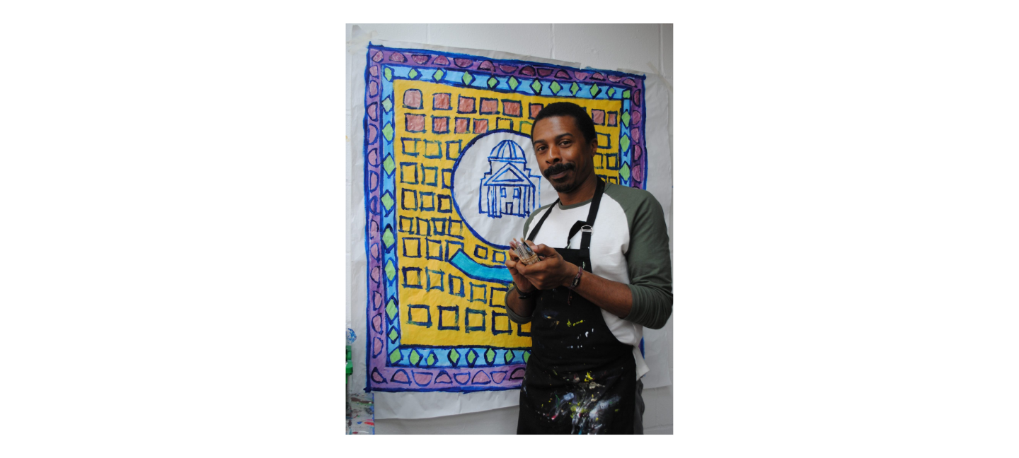 Thompson Hall stands in front of his artwork holding paintings in his hands.