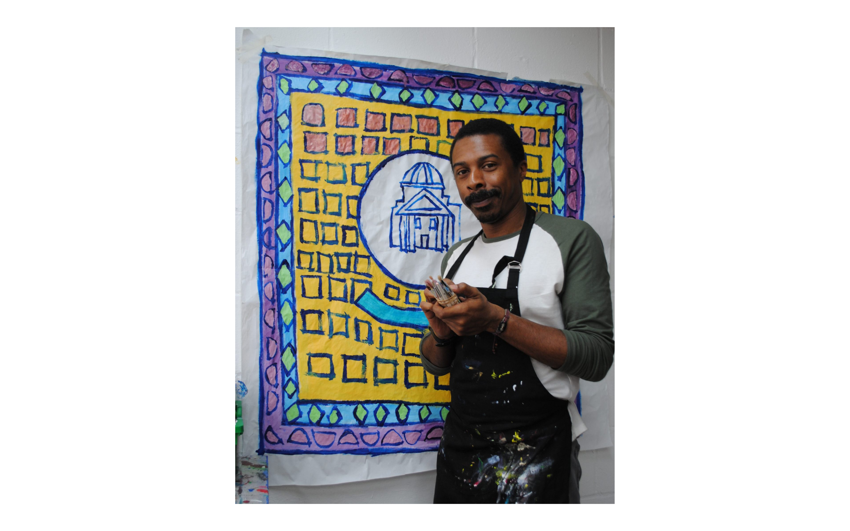 Thompson Hall stands in front of his artwork holding paintings in his hands.