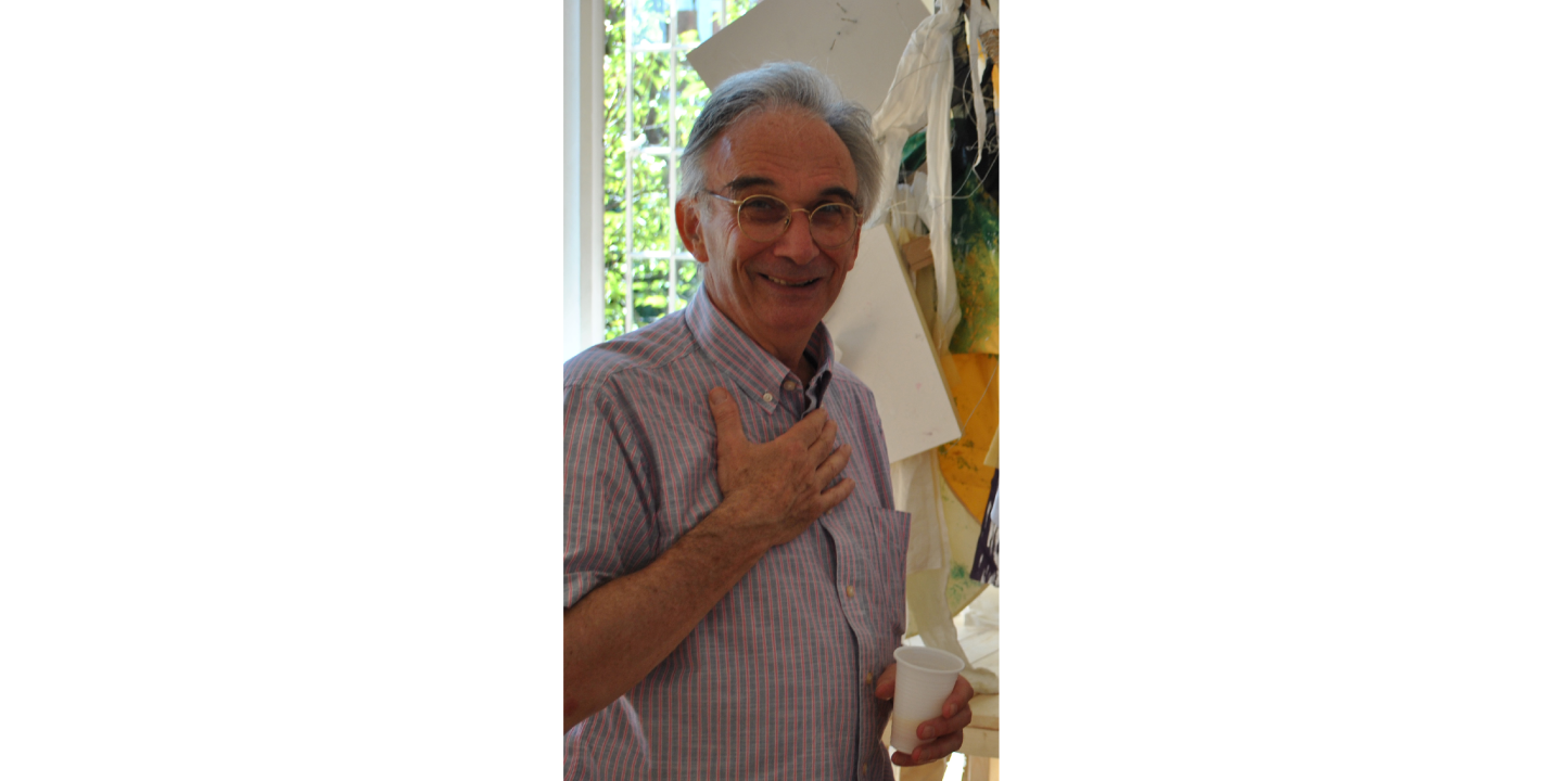 A portrait of a man with his right hand against his chest and a white plastic cup in his left hand.