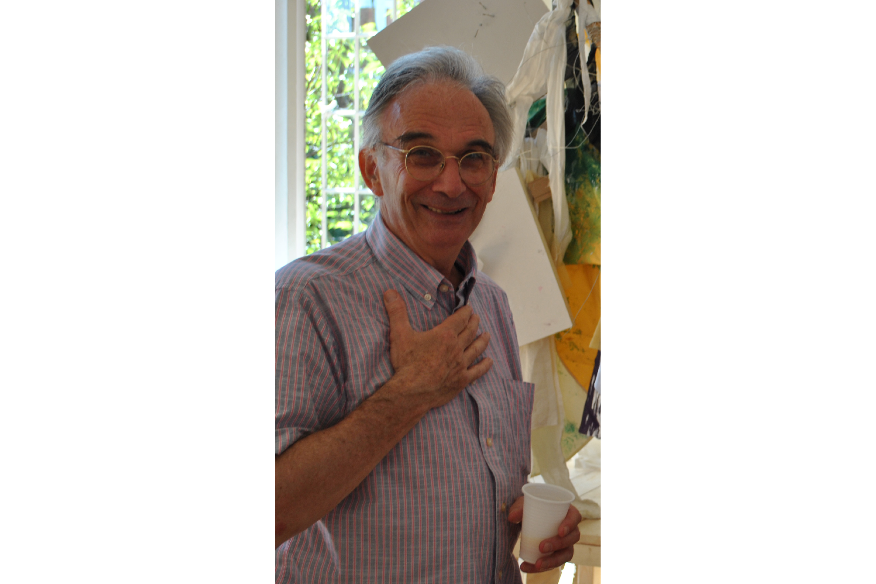 A portrait of a man with his right hand against his chest and a white plastic cup in his left hand.