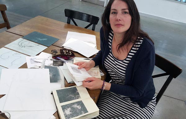 A woman looks up. She is sat at a table with a book in front of her.