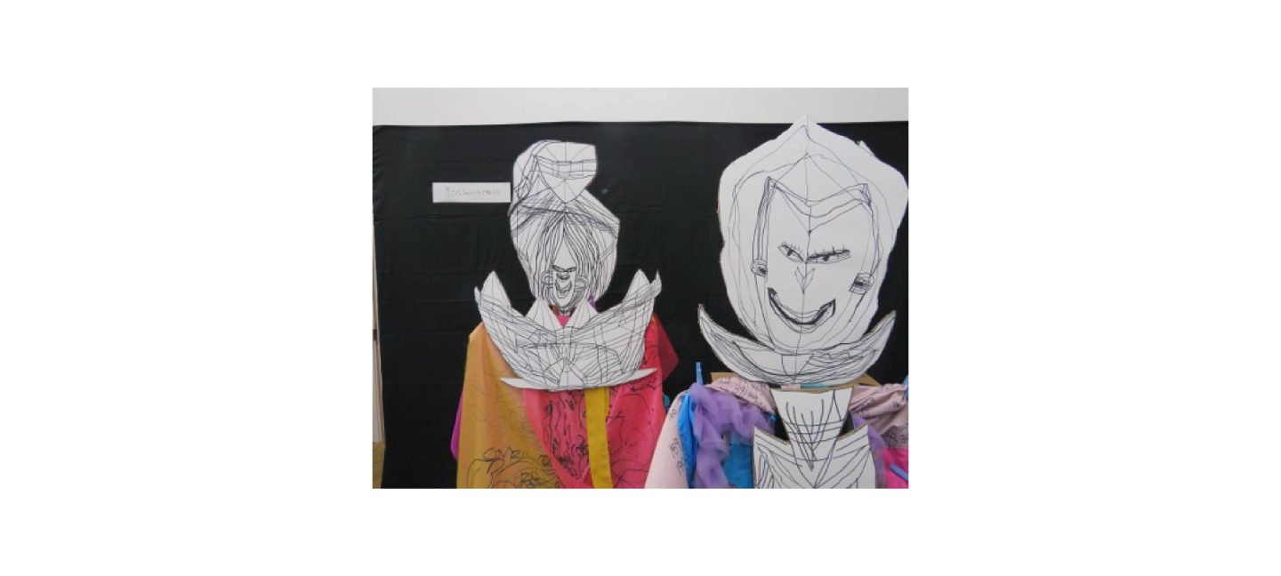 Two people wearing paper masks with black line drawing, whilst draped in colourful fabrics that have pens marks on.