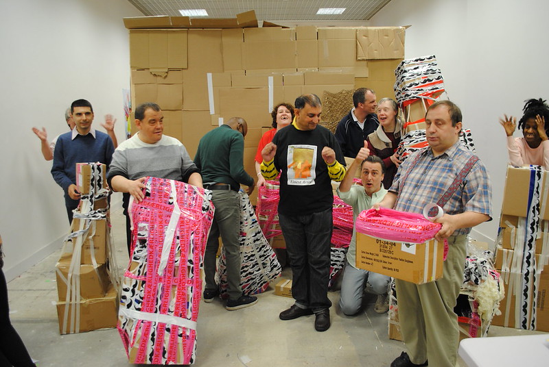 Pardip Kapil's workshop. He is in a room with other participants, holding cardboard boxes with colourful tape on them.