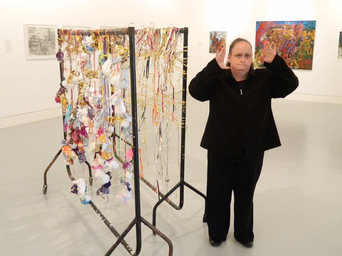 Artist Linda Bell, in an exhibition space, stood next to her artwork made of two black clothing rails with strings of fabric bunting hanging from them.
