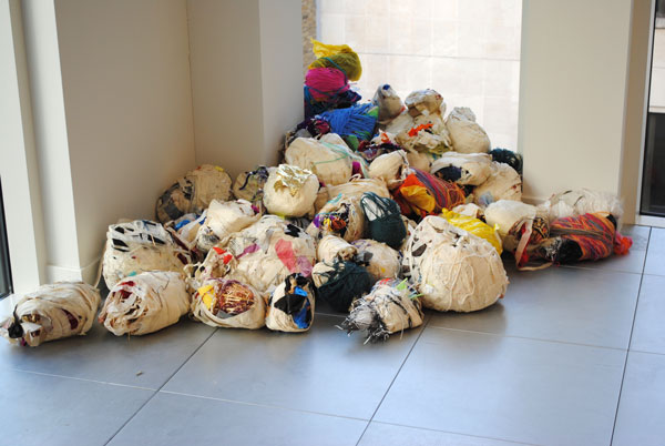A sculptural artwork made up of bundles of wrapped textiles piled together in a corner.