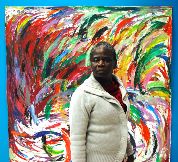 A woman stands in front of an abstract artwork made up of overlapping arcs brushstrokes painted in different colours.