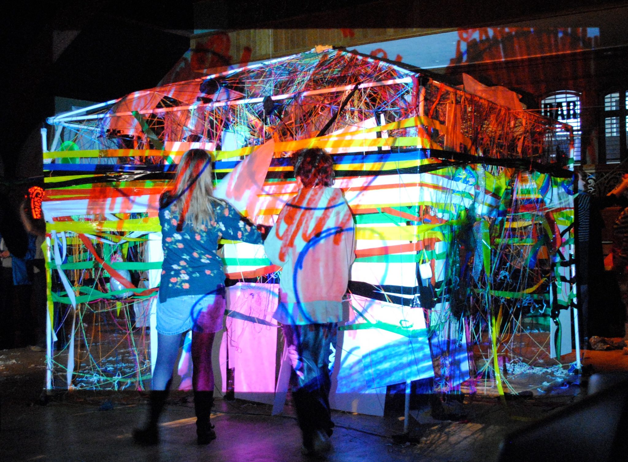 Two people stand in front of a projector, with colourful sketchy marks on the image.